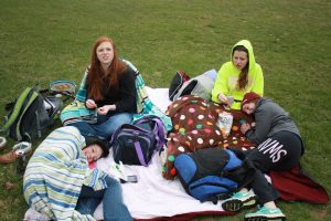 Tennis players Claire Pettinger, Kate Lynott, Riley Clark, and Erin Belding snuggle up in blankets and sweatshirts to combat the cold weather in the 40s for their meet against Western Dubuque on April 15. Photo By Grayson Snyder. 