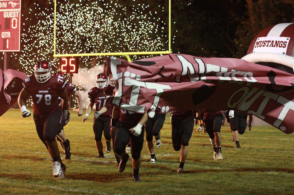 Before the game, football players break through the cheer banner as fireworks go off in the background. Photo by Emma Klinkhammer