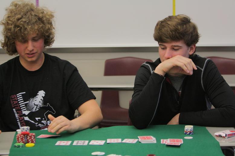 Seniors Drew Wolfe and Aaron Barnhart study the cards flipped in a game of poker in Are You Game? Photo by Cale Snedden.