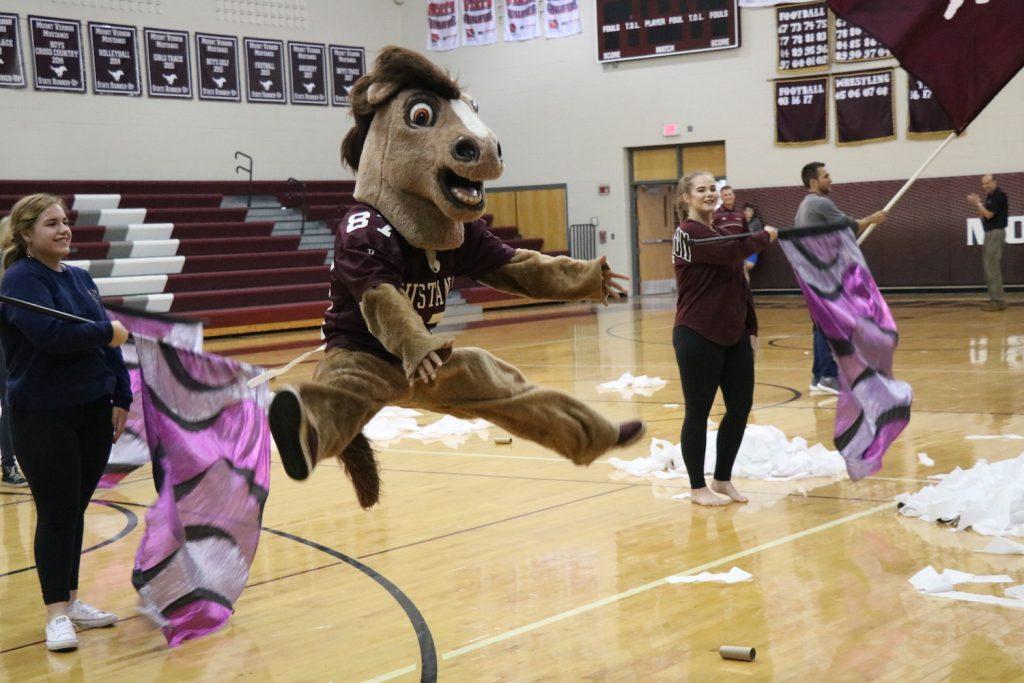 Junior Jaruthat Dervo, dressed as the school mascot, does a toe touch during the fight song at the pep assembly on Sept. 28. Photo by Lillie Hawker.