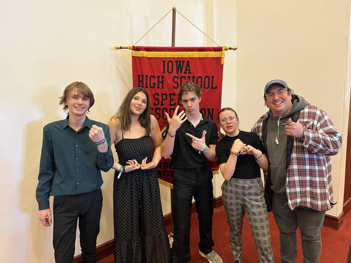 Grant Tucker, Cait OConner, Kevin Zhems,  Skye Rodman, and Coach Trevor Baty pose in front of the All-State banner after performing their piece We´re All Chickens in the End. 