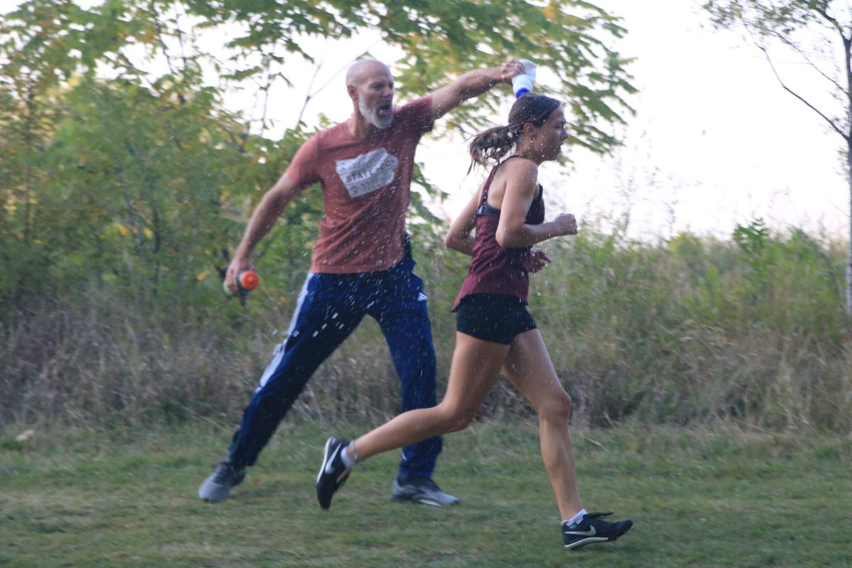 Junior Cora Smith runs past her dad as he pours water on her head in the varsity race at the Ames meet Sept. 5.  