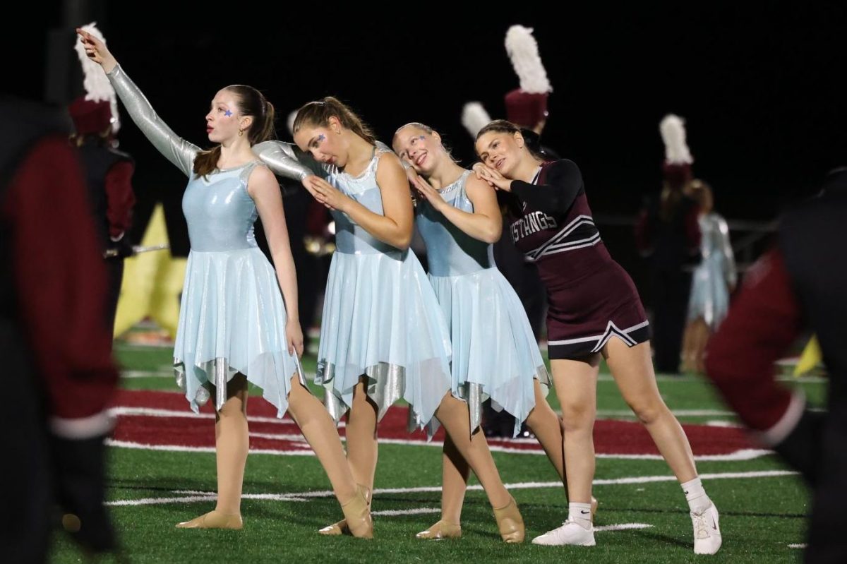 Color guard member junior Malena Koehn, along with seniors Isabella Hasley, Natalie Theurauf, and Emma Houghtaling, pose together during the marching band's performance. 