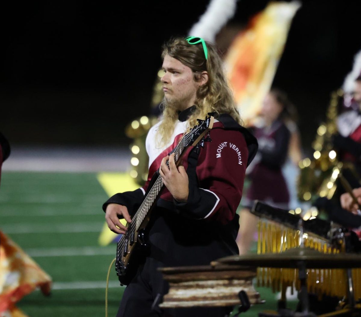 Senior Nick Alles watches the drum major as he plays his guitar with the marching band.