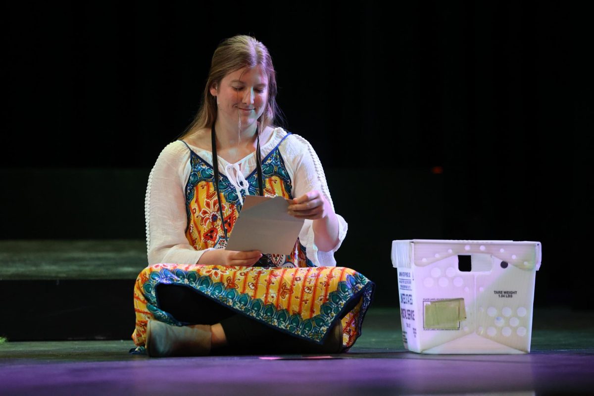 Senior Selah Loyd, acting as Yolie, smiles as she opens mail. 