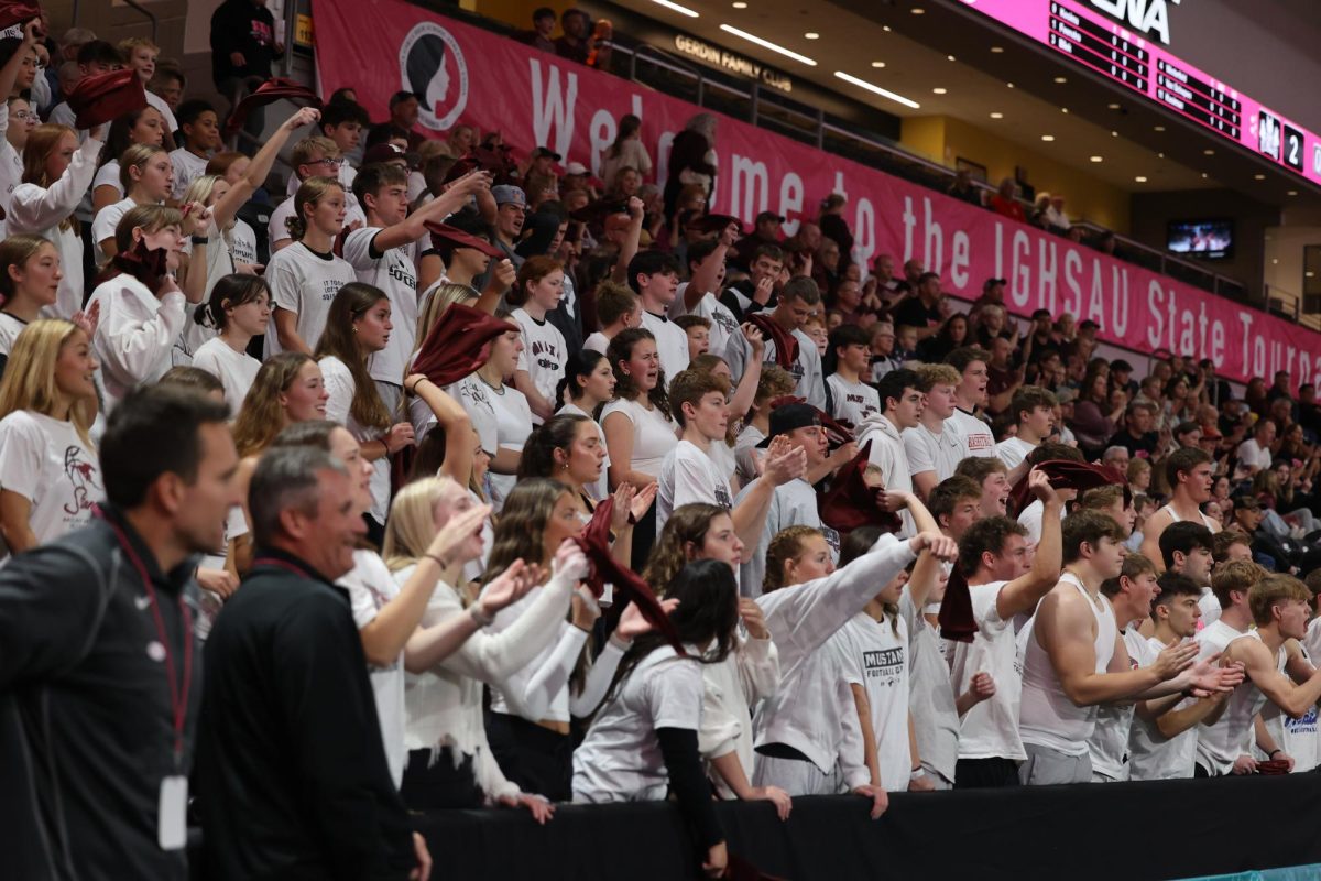 The Mount Vernon student section enthusiastically cheers and waves maroon flags in support of their volleyball team.