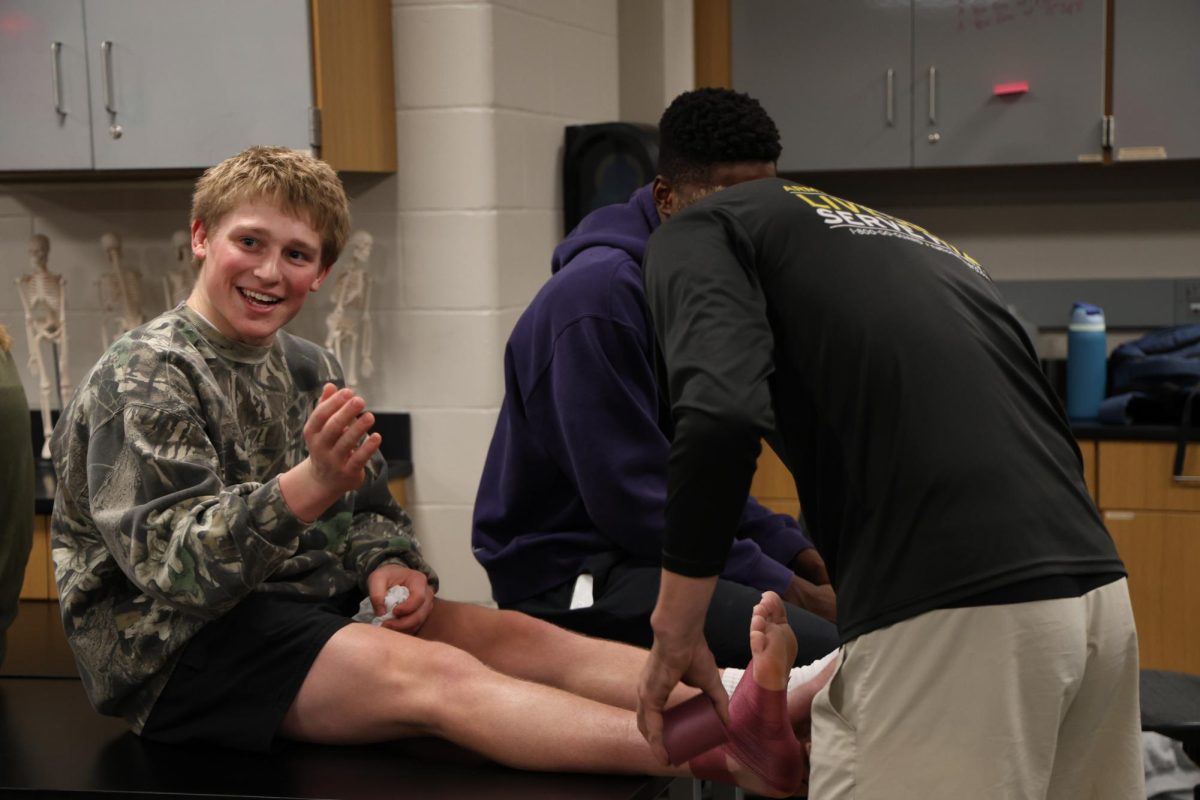 Sophomore Nolan Mercer smiles at a classmate while junior LJ Korte tapes his ankle in the Exercise Science J-term Jan. 7.