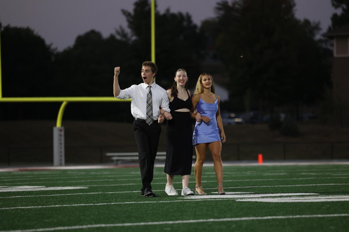 Court members Kevin Zehms and Taylor Franck take the field with a senior student council member, Malena Koehn. Kevin pumps his fist in celebration of his accomplishments being announced before the crowning on Oct. 2. 