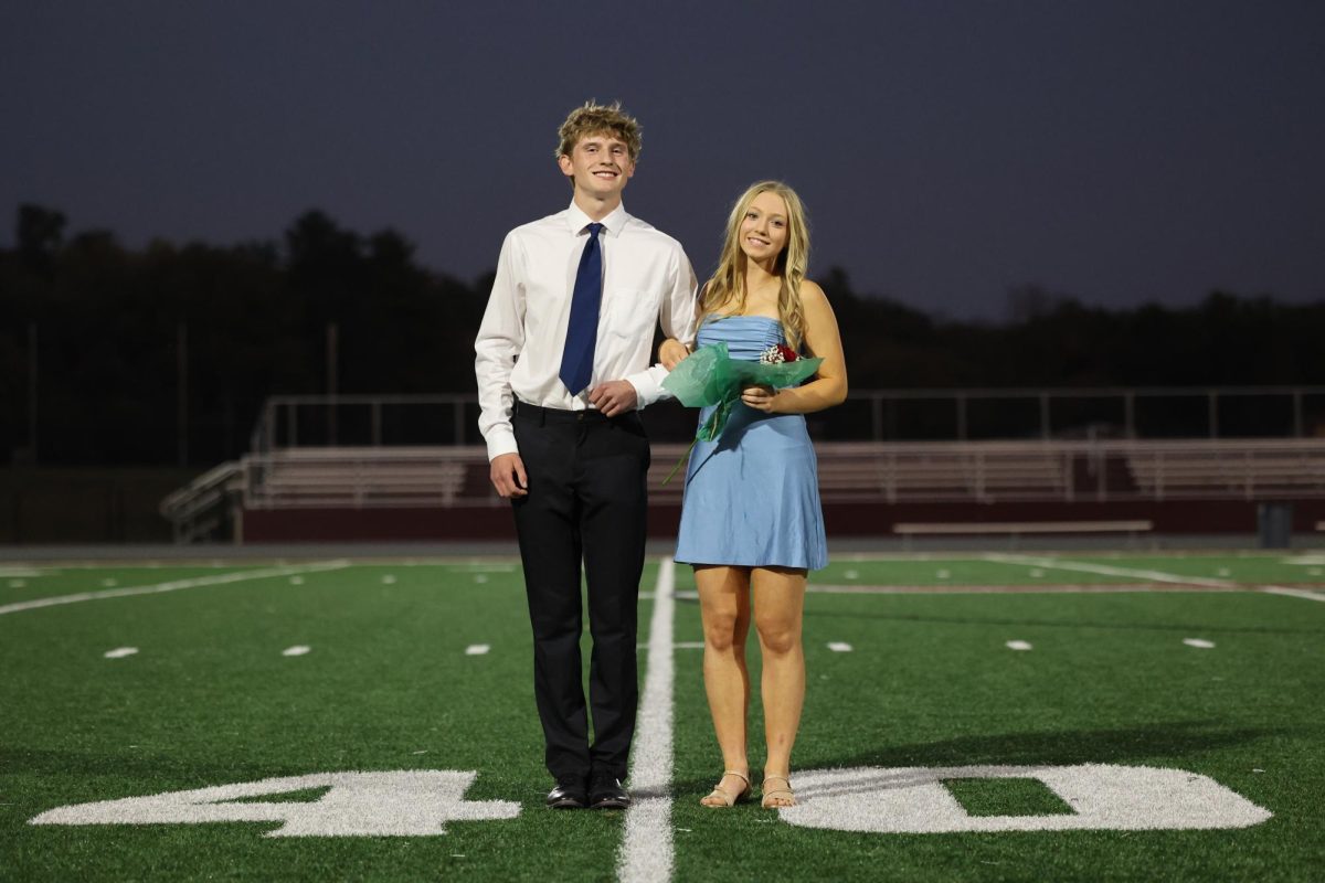 Seniors Nathan Conrad and Isabelle Logue smile for a photo after figuring out how to link arms after taking the field as homecoming royalty on Oct. 2. 